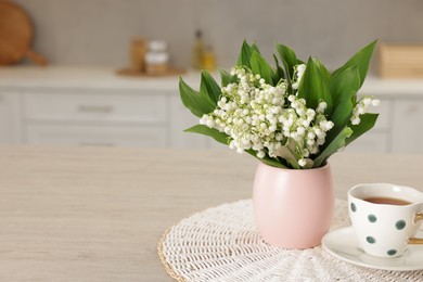 Photo of Bouquet of beautiful lily-of-the-valley and cup of tea on wooden table in kitchen, closeup. Space for text