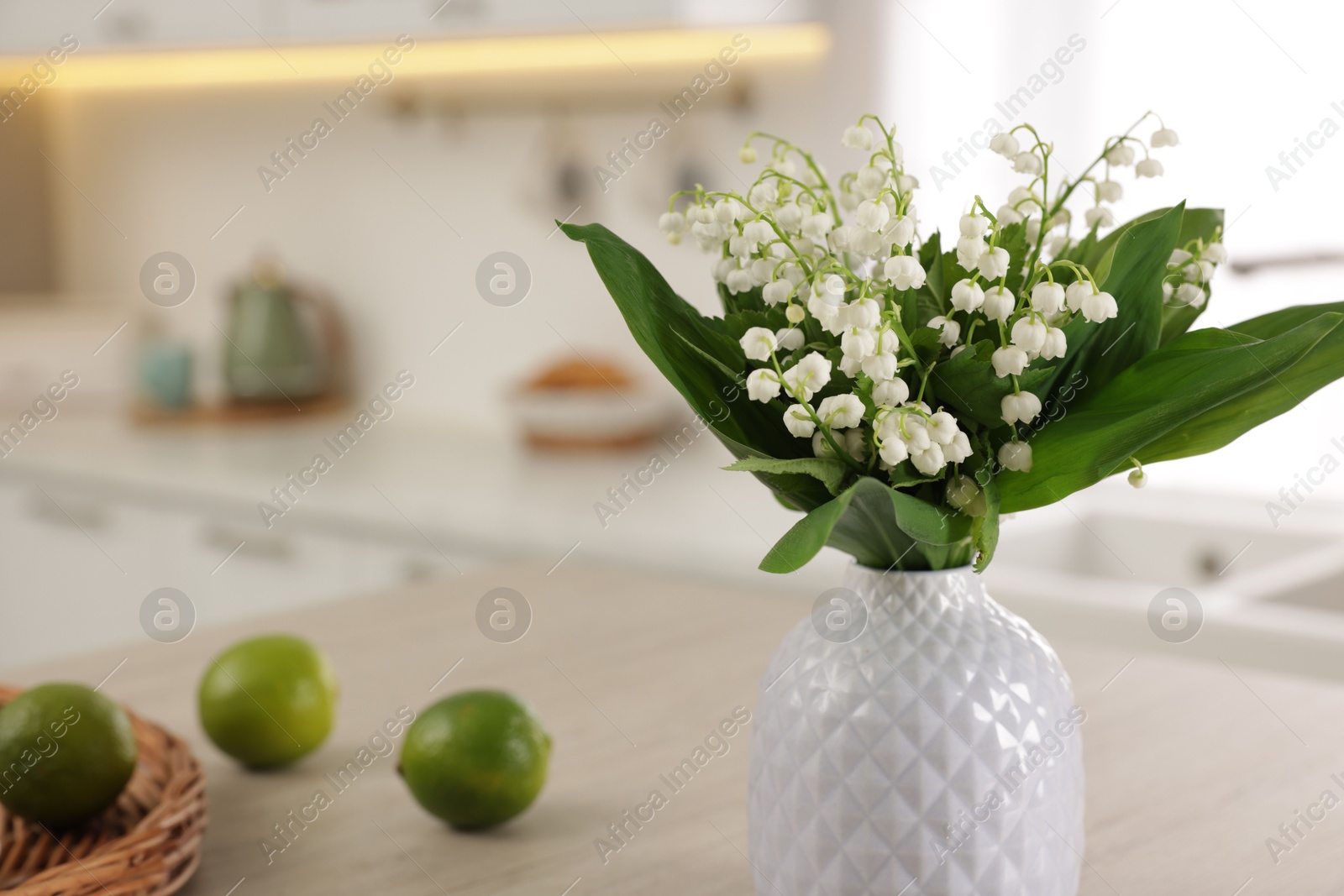 Bouquet of beautiful lily-of-the-valley in vase and limes on table indoors, closeup Photo of Bouquet of beautiful lily-of-the-valley in vase and limes on table indoors, closeup