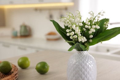 Photo of Bouquet of beautiful lily-of-the-valley in vase and limes on table indoors, closeup