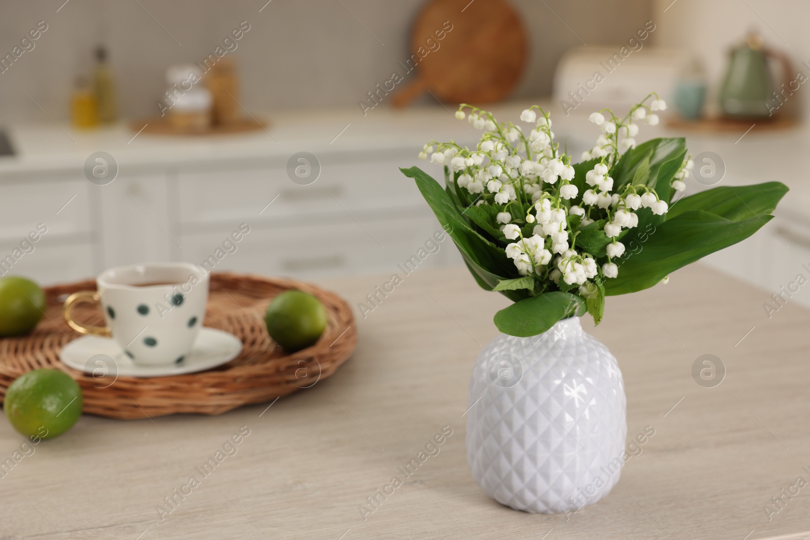 Beautiful lily-of-the-valley in vase, limes and cup of tea on wooden table in kitchen, closeup Photo of Beautiful lily-of-the-valley in vase, limes and cup of tea on wooden table in kitchen, closeup