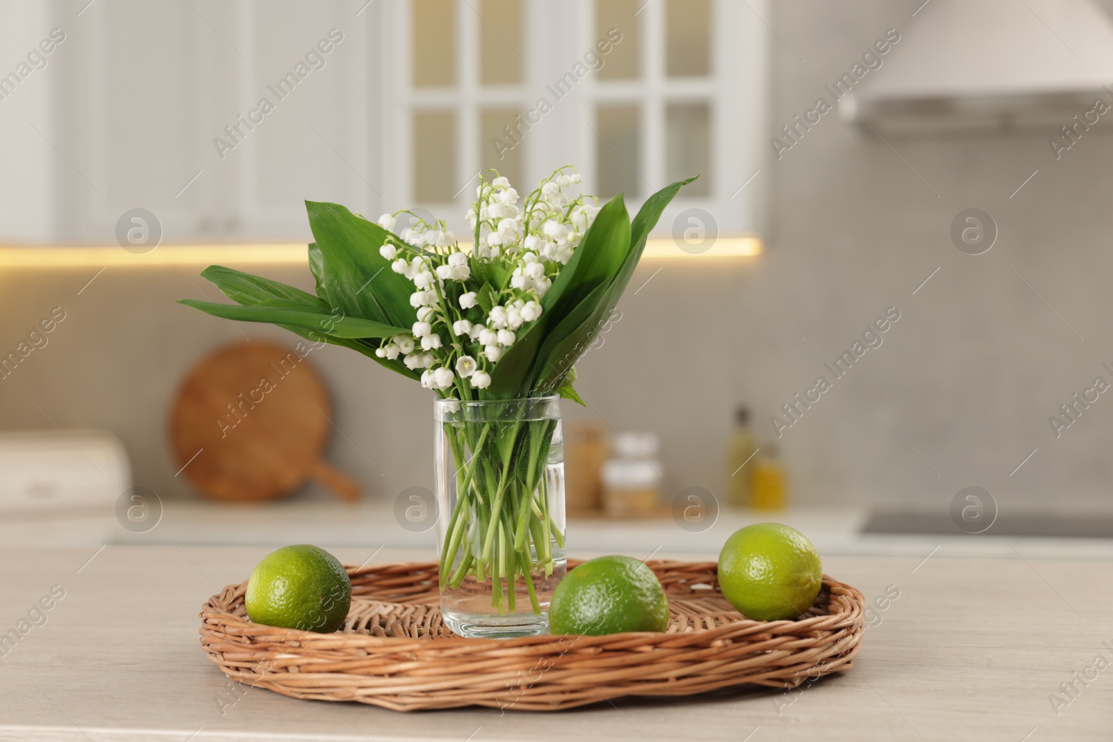 Bouquet of beautiful lily-of-the-valley and limes on wooden table in kitchen, closeup Photo of Bouquet of beautiful lily-of-the-valley and limes on wooden table in kitchen, closeup