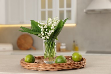 Photo of Bouquet of beautiful lily-of-the-valley and limes on wooden table in kitchen, closeup