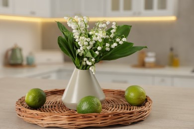Photo of Bouquet of beautiful lily-of-the-valley in vase and limes on wooden table in kitchen, closeup