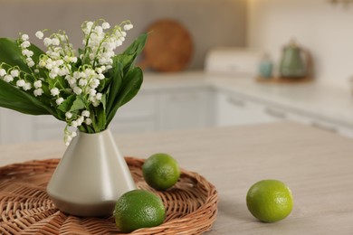 Photo of Bouquet of beautiful lily-of-the-valley in vase and limes on wooden table in kitchen, closeup. Space for text