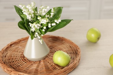 Photo of Bouquet of beautiful lily-of-the-valley in vase and apples on wooden table indoors, closeup