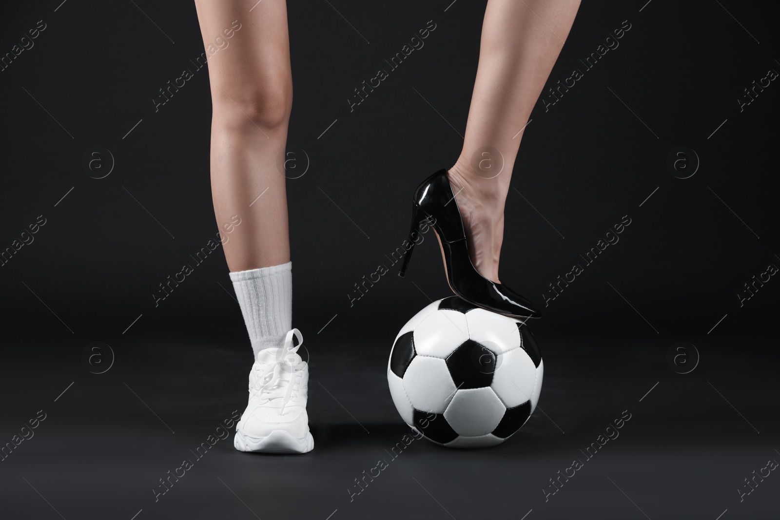 Woman in high heeled shoe and sneaker with soccer ball on dark background, closeup Photo of Woman in high heeled shoe and sneaker with soccer ball on dark background, closeup