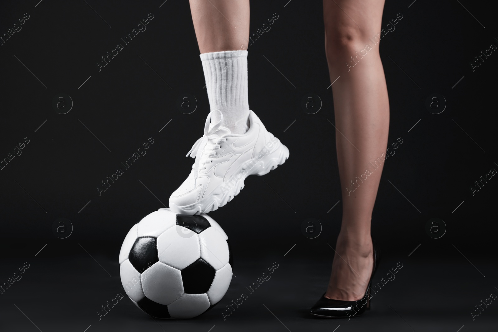 Woman in high heeled shoe and sneaker with soccer ball on dark background, closeup Photo of Woman in high heeled shoe and sneaker with soccer ball on dark background, closeup