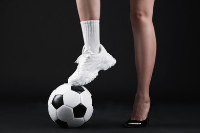 Photo of Woman in high heeled shoe and sneaker with soccer ball on dark background, closeup