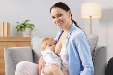 Photo of Smiling mother breastfeeding her little baby on armchair indoors