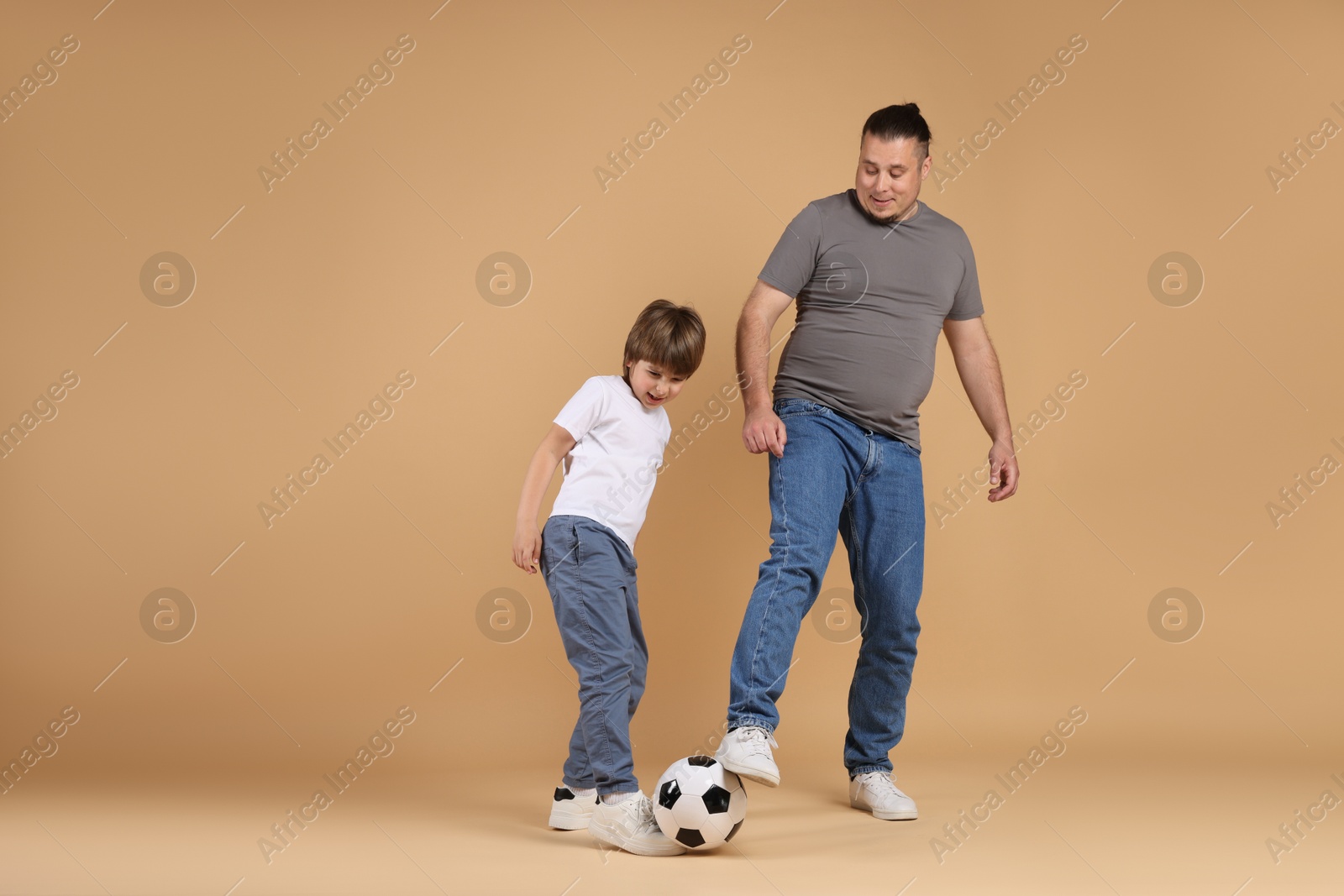 Father and his son playing football on beige background Photo of Father and his son playing football on beige background