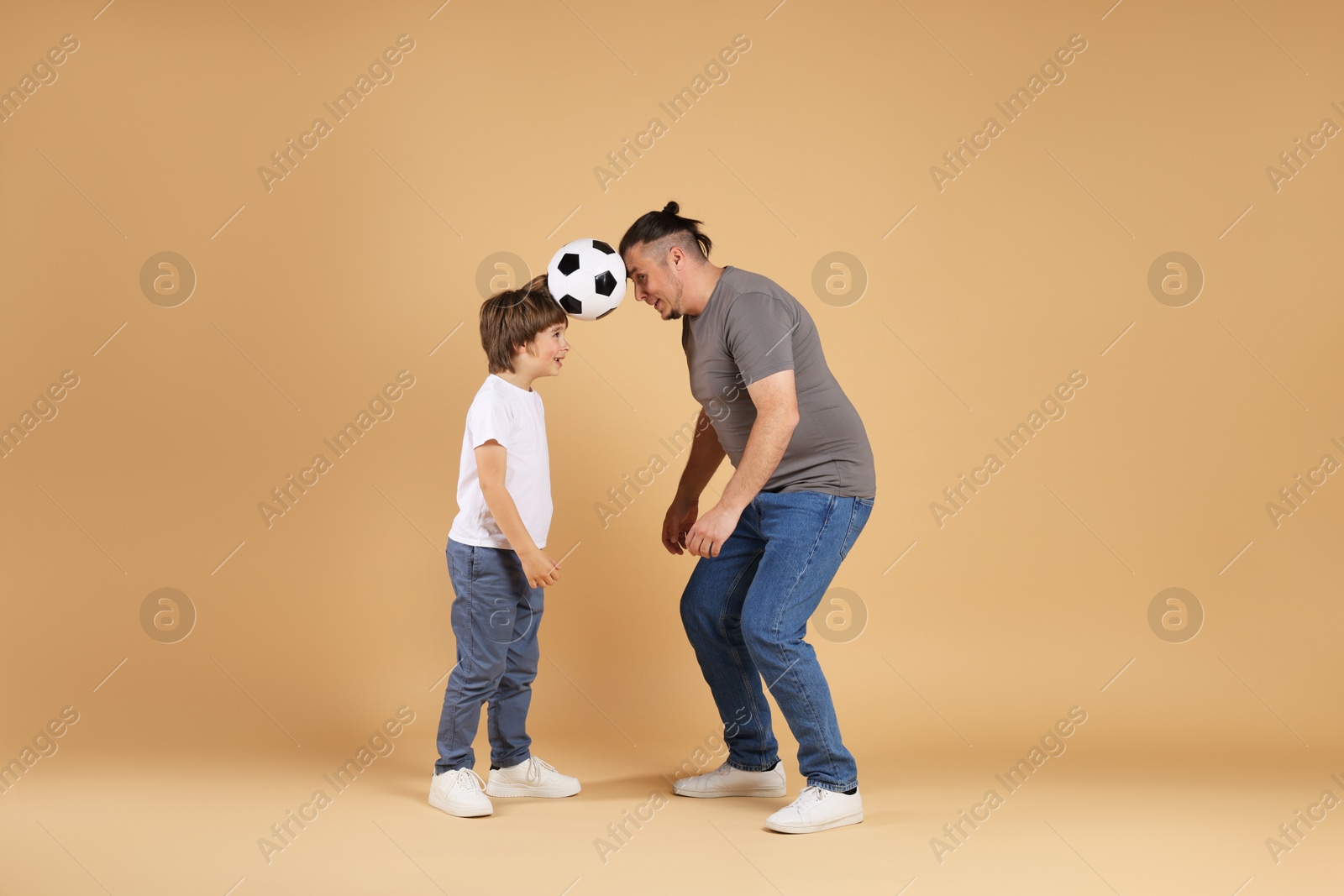 Father and his son playing football on beige background Photo of Father and his son playing football on beige background