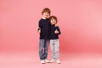 Photo of Cute little brothers showing thumbs ups on pink background