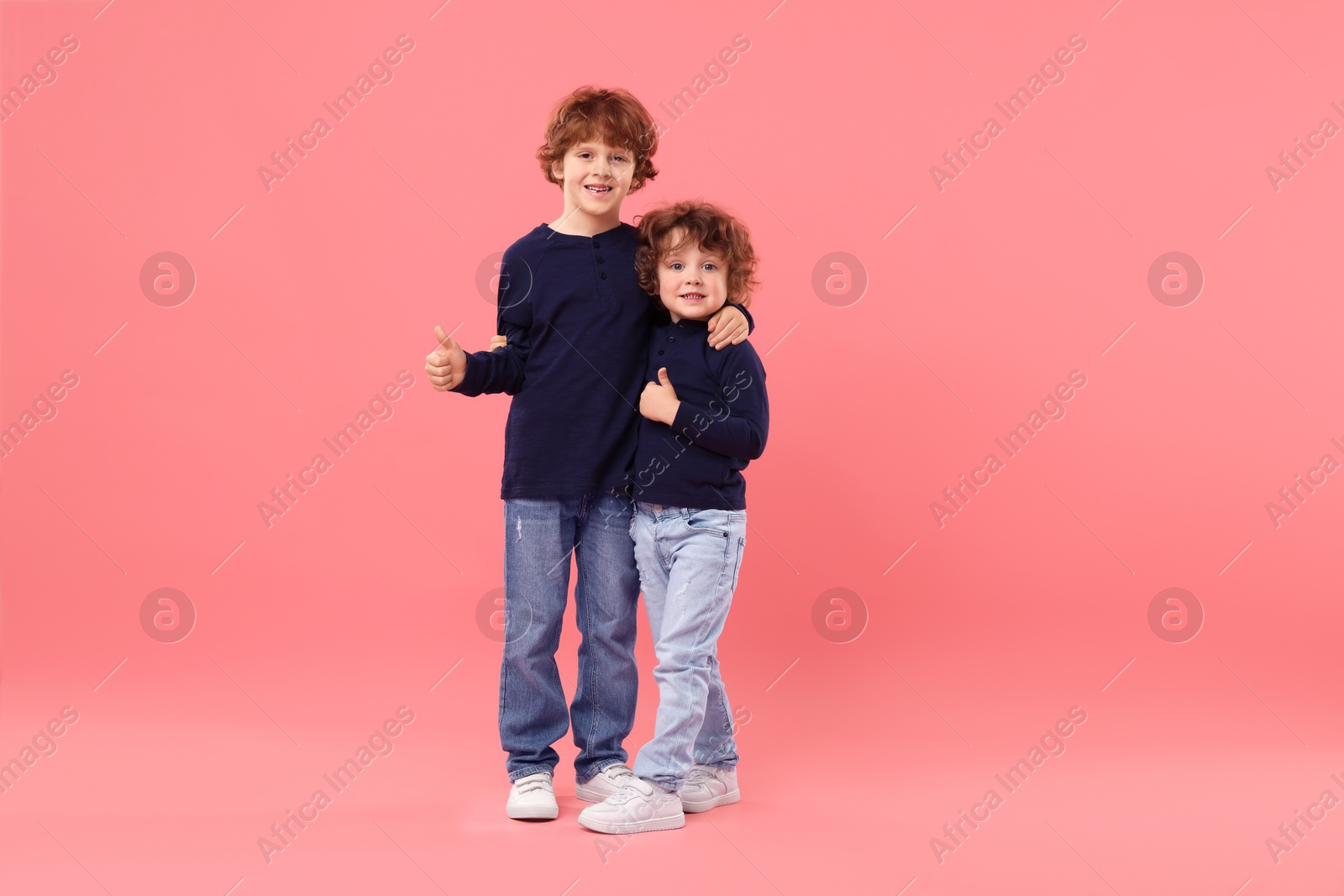 Cute little brothers showing thumbs ups on pink background Photo of Cute little brothers showing thumbs ups on pink background