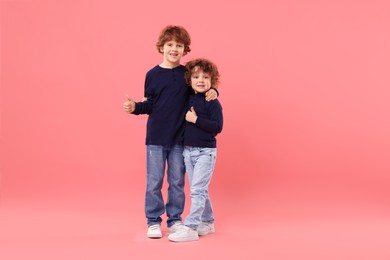 Photo of Cute little brothers showing thumbs ups on pink background