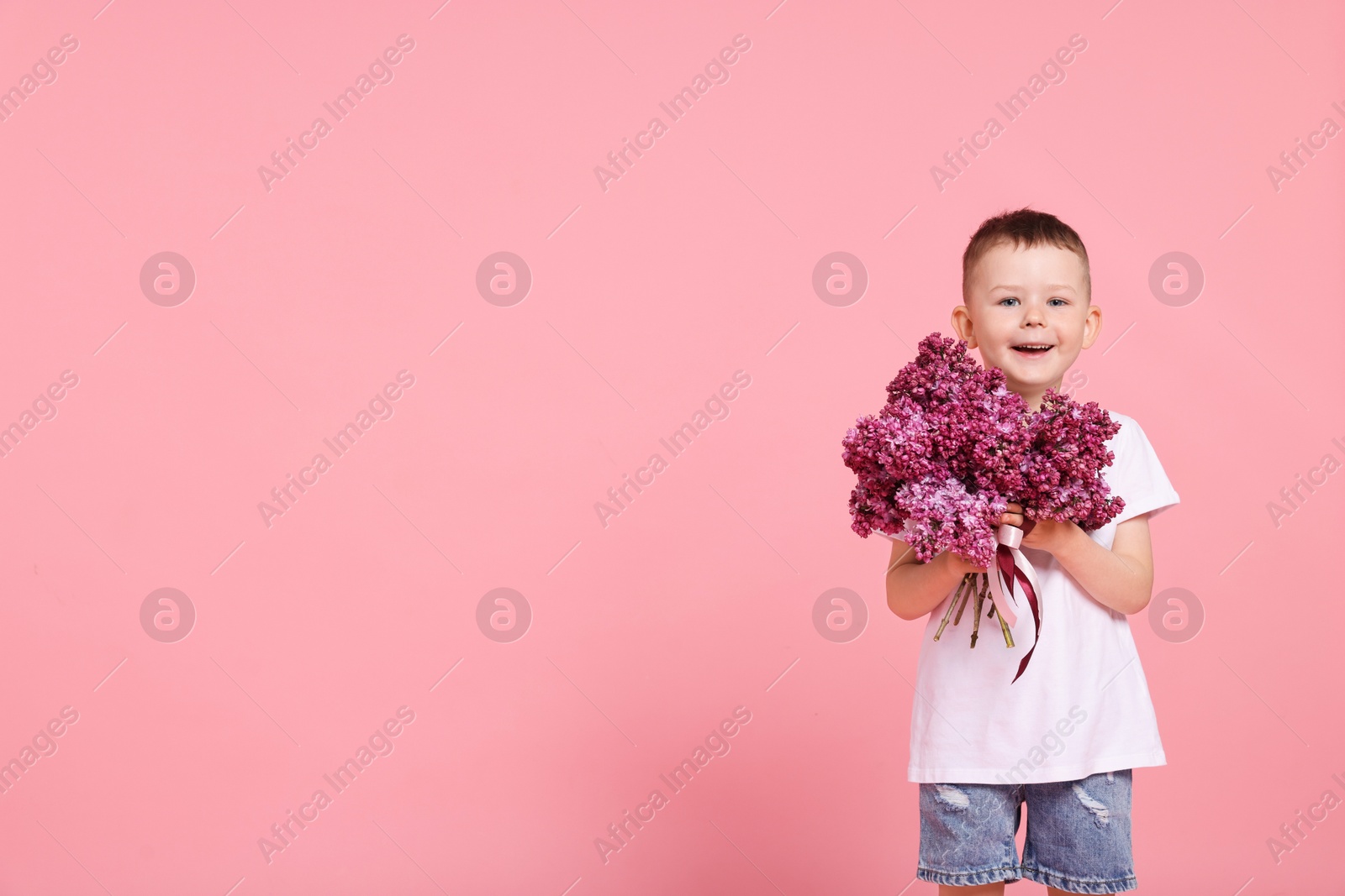 Little boy with bouquet of lilac flowers on pink background, space for text Photo of Little boy with bouquet of lilac flowers on pink background, space for text