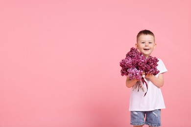 Photo of Little boy with bouquet of lilac flowers on pink background, space for text