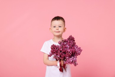 Photo of Little boy with bouquet of lilac flowers on pink background