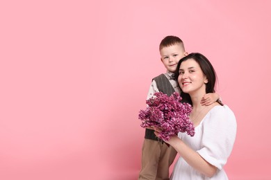 Photo of Mother and her son with bouquet of lilac flowers on pink background, space for text