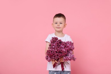Photo of Little boy with bouquet of lilac flowers on pink background