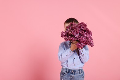 Photo of Little boy with bouquet of lilac flowers on pink background, space for text