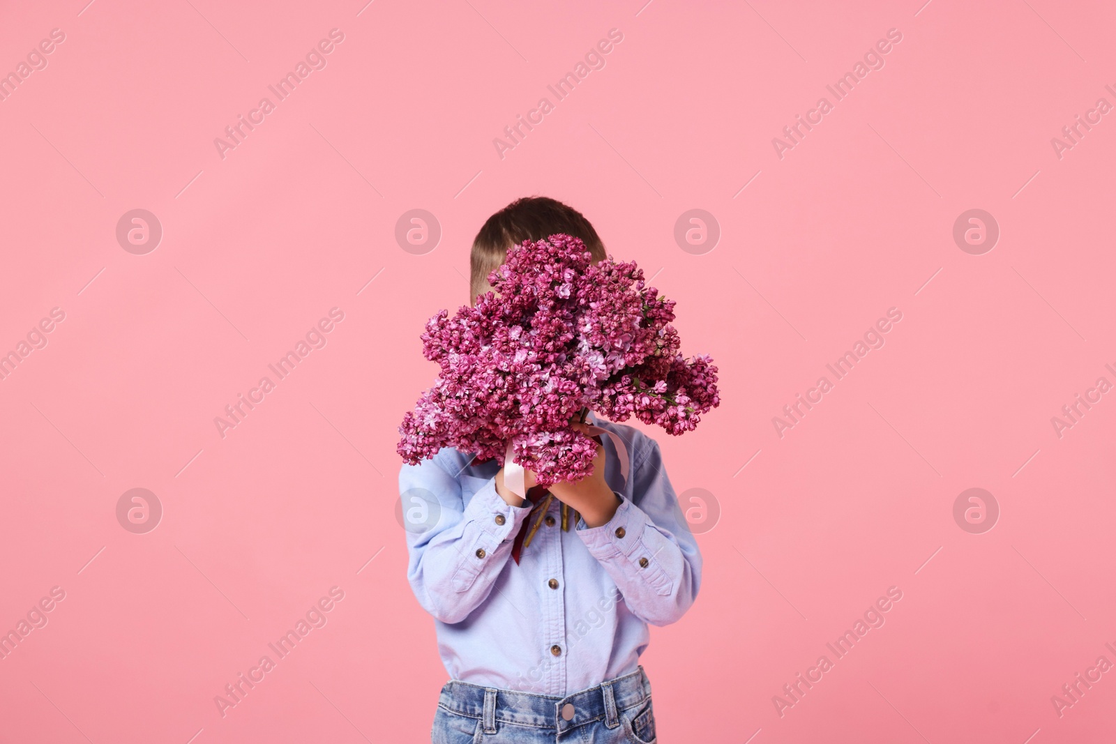 Little boy with bouquet of lilac flowers on pink background Photo of Little boy with bouquet of lilac flowers on pink background