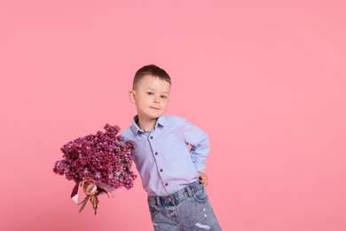 Photo of Little boy with bouquet of lilac flowers on pink background, space for text