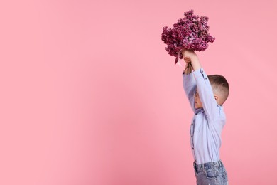 Photo of Little boy with bouquet of lilac flowers on pink background, space for text