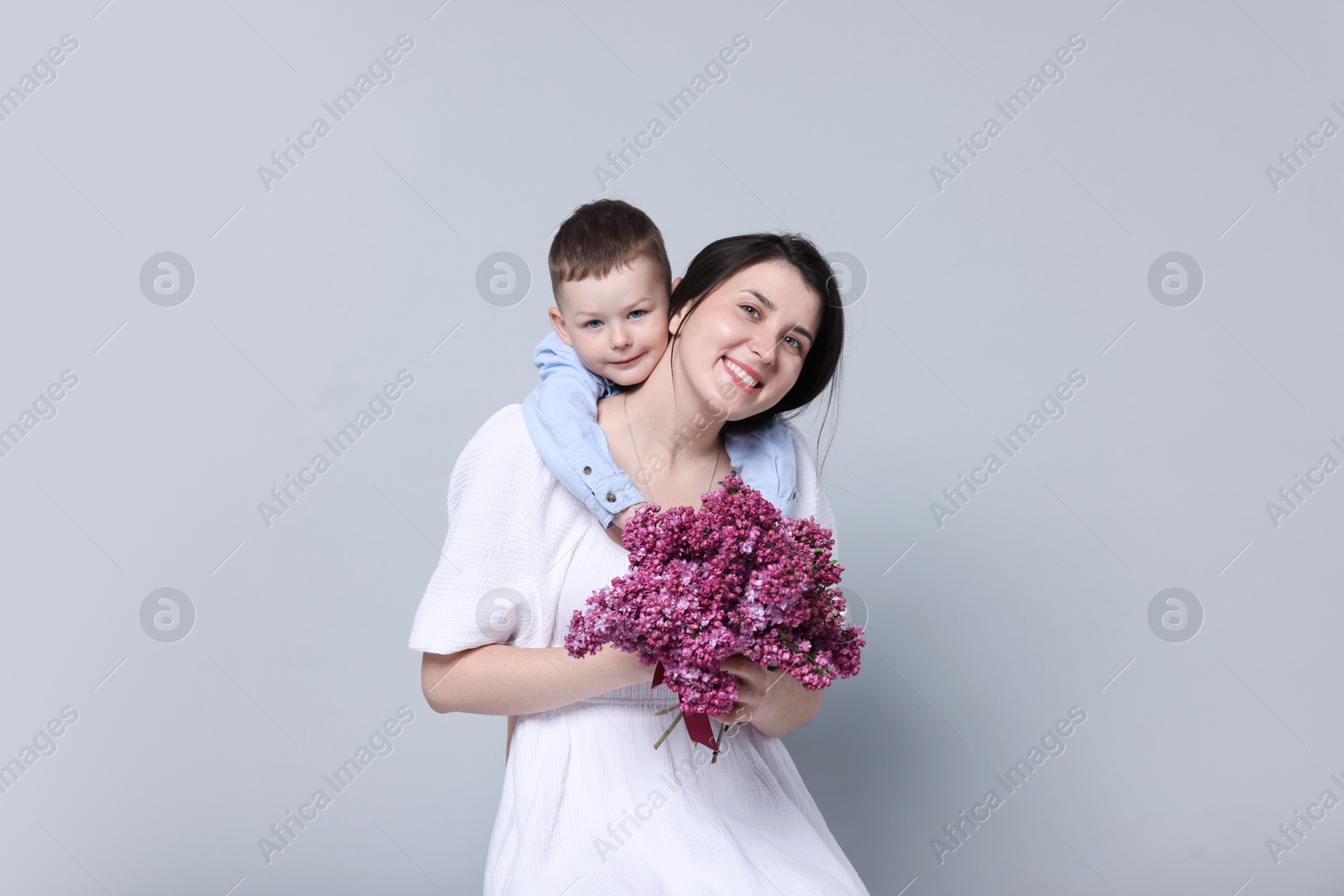 Mother and her son with bouquet of lilac flowers on light grey background Photo of Mother and her son with bouquet of lilac flowers on light grey background
