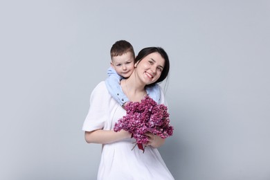 Photo of Mother and her son with bouquet of lilac flowers on light grey background