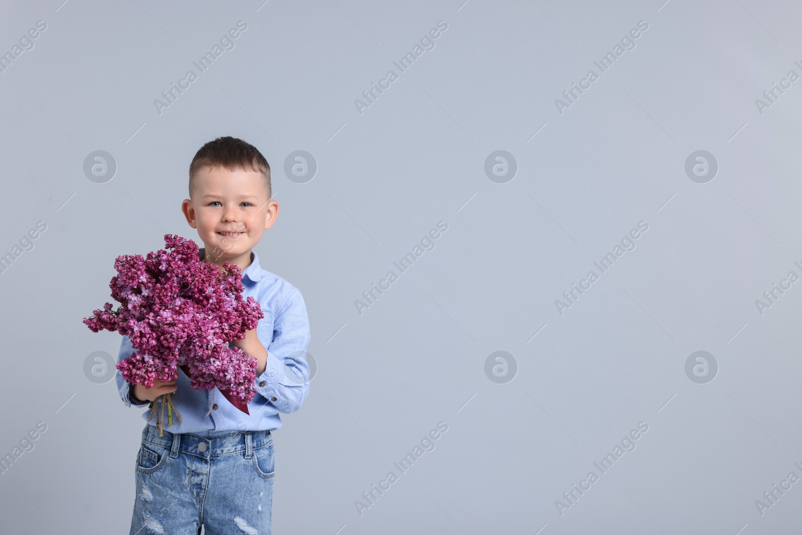 Little boy with bouquet of lilac flowers on light grey background, space for text Photo of Little boy with bouquet of lilac flowers on light grey background, space for text