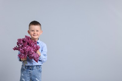 Photo of Little boy with bouquet of lilac flowers on light grey background, space for text