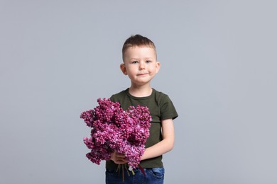 Photo of Little boy with bouquet of lilac flowers on light grey background