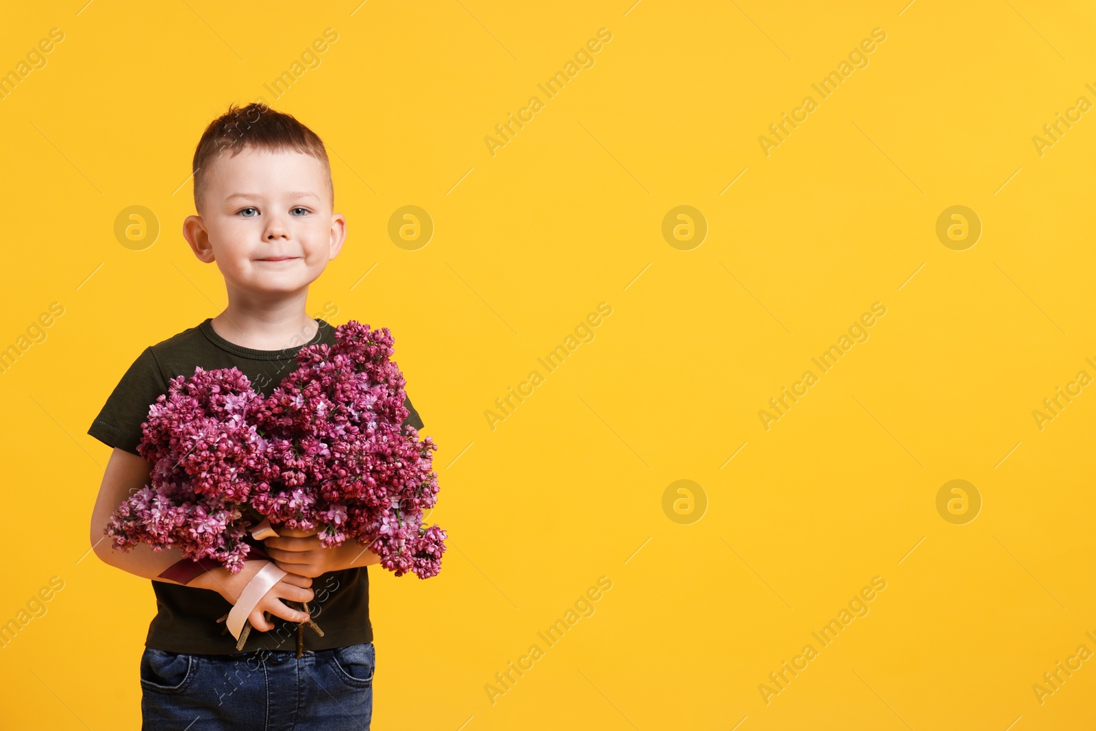 Little boy with bouquet of lilac flowers on yellow background, space for text Photo of Little boy with bouquet of lilac flowers on yellow background, space for text