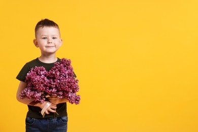 Photo of Little boy with bouquet of lilac flowers on yellow background, space for text