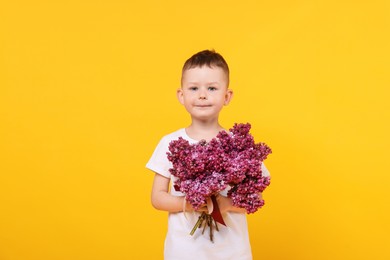 Photo of Little boy with bouquet of lilac flowers on yellow background