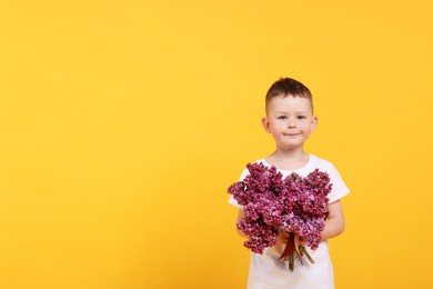 Photo of Little boy with bouquet of lilac flowers on yellow background, space for text