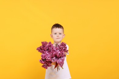 Photo of Little boy with bouquet of lilac flowers on yellow background