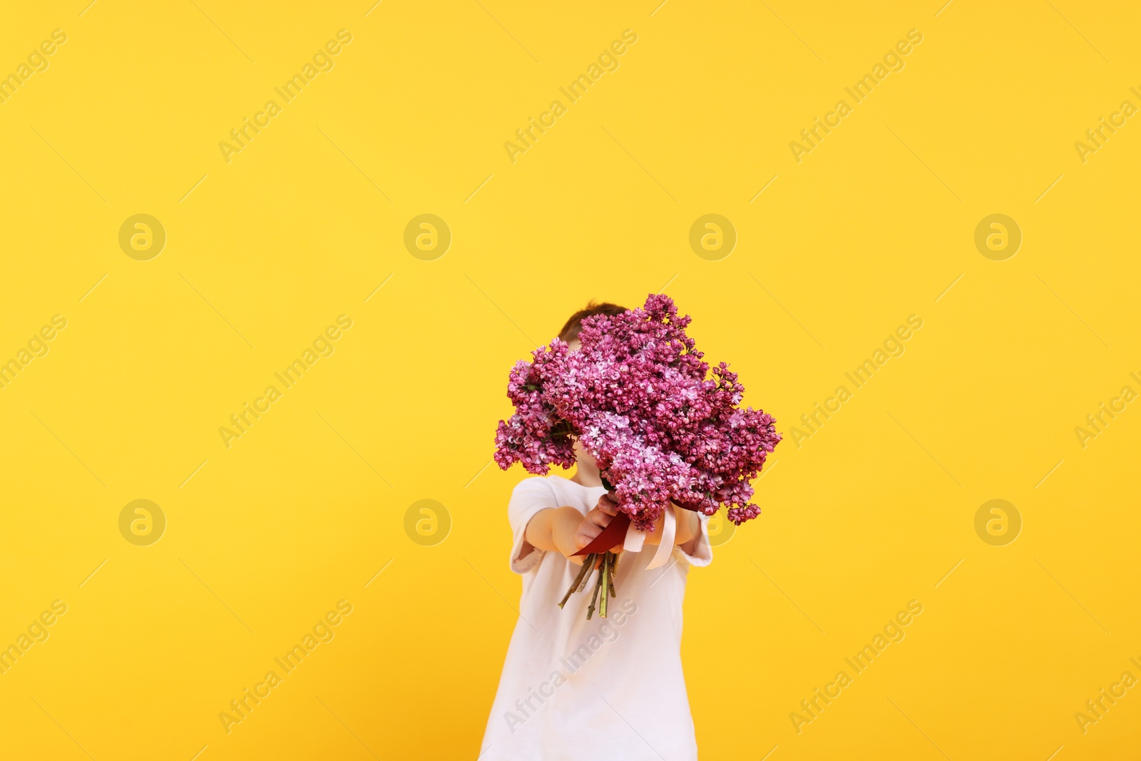 Little boy with bouquet of lilac flowers on yellow background Photo of Little boy with bouquet of lilac flowers on yellow background