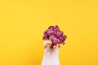 Photo of Little boy with bouquet of lilac flowers on yellow background