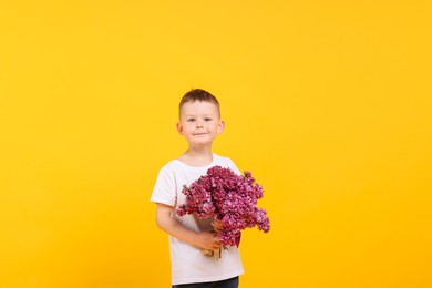 Photo of Little boy with bouquet of lilac flowers on yellow background