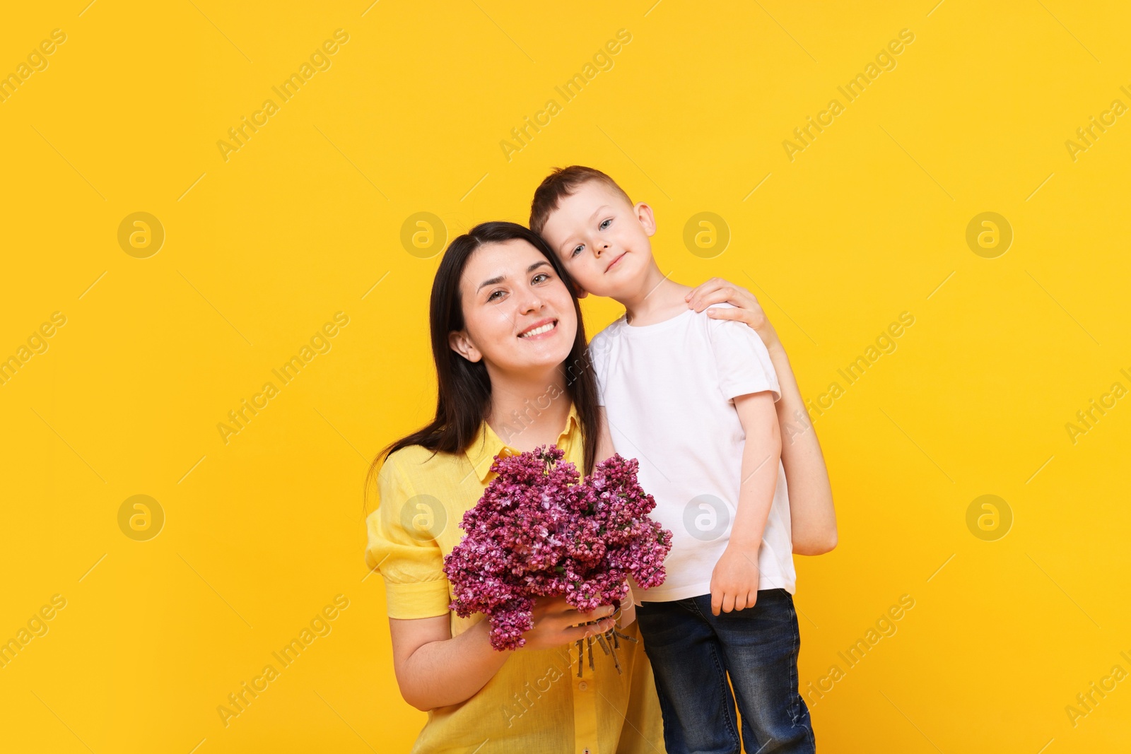 Mother and her son with bouquet of lilac flowers on yellow background Photo of Mother and her son with bouquet of lilac flowers on yellow background