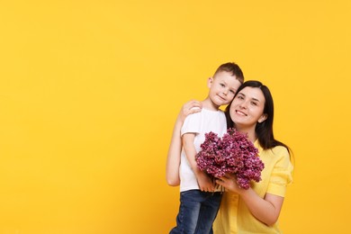 Photo of Mother and her son with bouquet of lilac flowers on yellow background, space for text