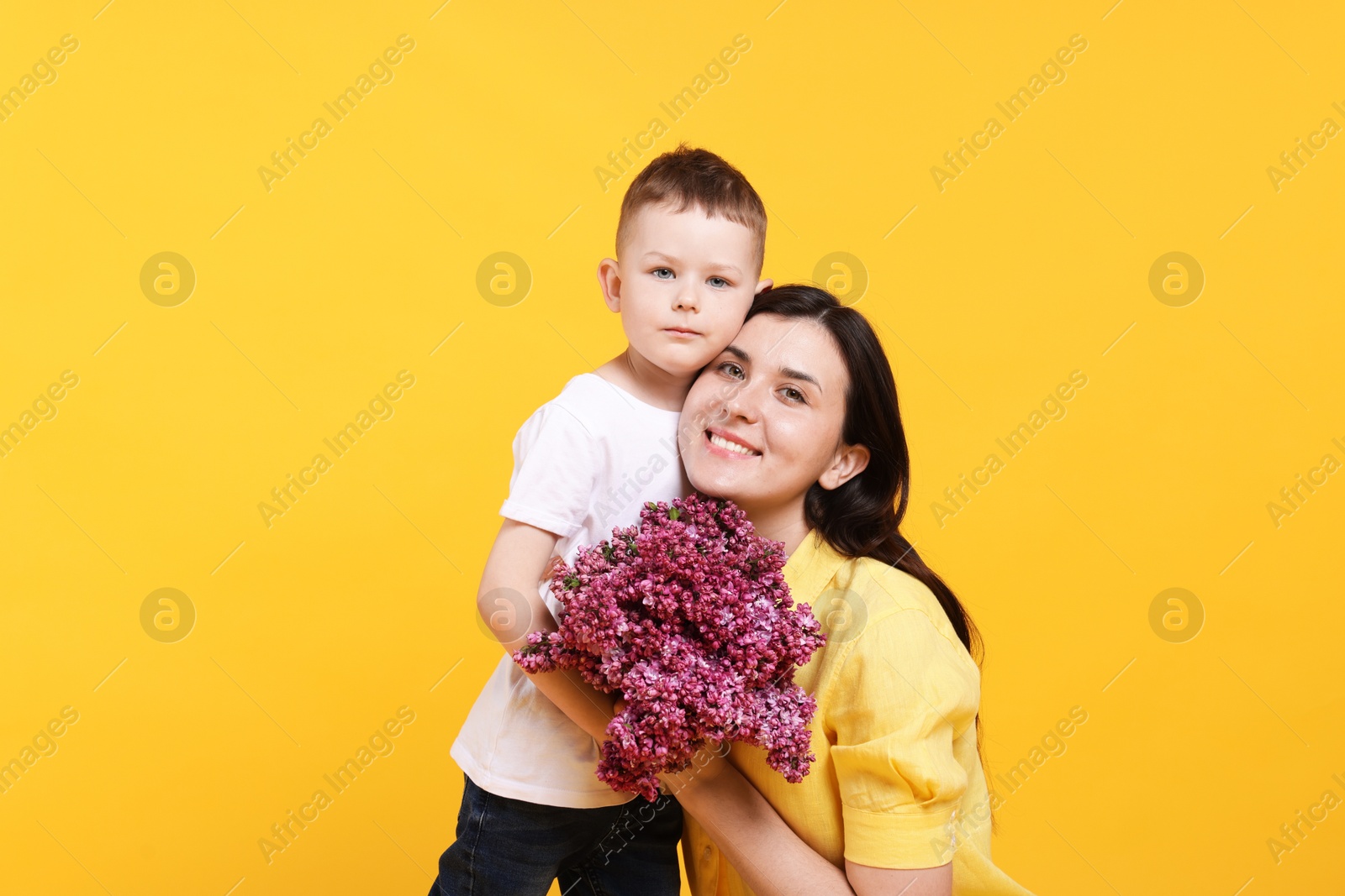 Mother and her son with bouquet of lilac flowers on yellow background Photo of Mother and her son with bouquet of lilac flowers on yellow background