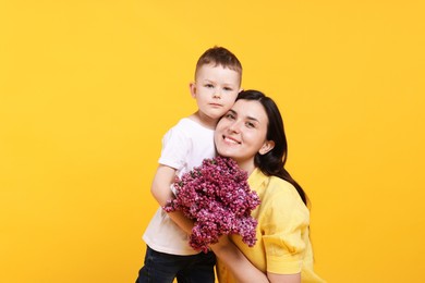 Photo of Mother and her son with bouquet of lilac flowers on yellow background