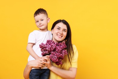 Photo of Mother and her son with bouquet of lilac flowers on yellow background, space for text