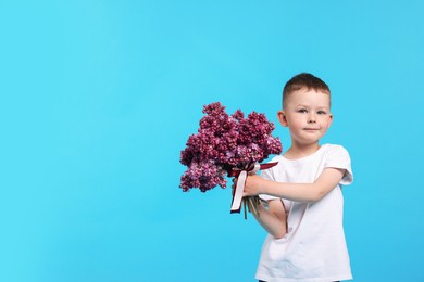 Photo of Little boy with bouquet of lilac flowers on light blue background, space for text