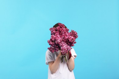 Photo of Little boy with bouquet of lilac flowers on light blue background