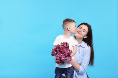 Photo of Mother and her son with bouquet of lilac flowers on light blue background, space for text
