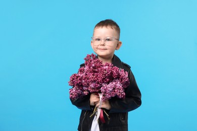 Photo of Little boy with bouquet of lilac flowers on light blue background