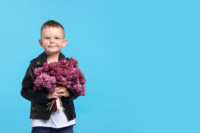 Photo of Little boy with bouquet of lilac flowers on light blue background, space for text